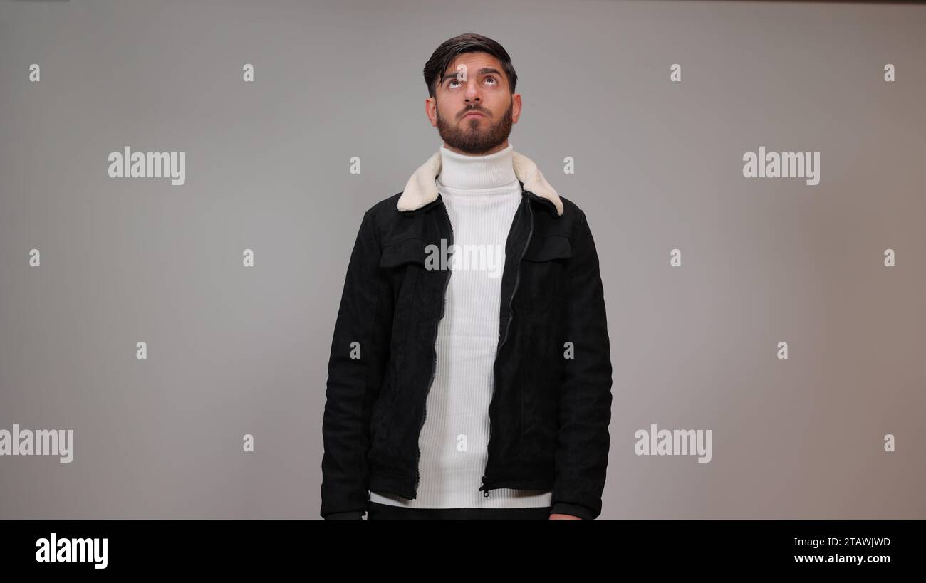 Ein verwirrter junger Mann, der vor grauem Hintergrund denkt. Stockfoto