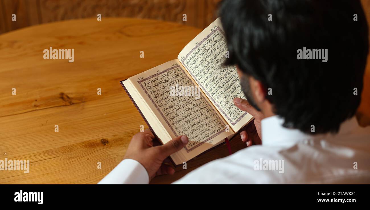 Muslimischer Mann, der den heiligen Koran liest. Der heilige Quran in der Hand mit arabischem Text, was Al Quran bedeutet. Stockfoto