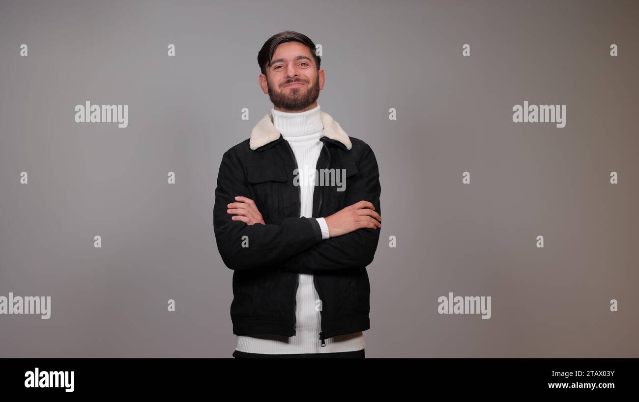 Ein junger Mann posiert mit stolzem Ausdruck vor grauem Hintergrund. Stockfoto