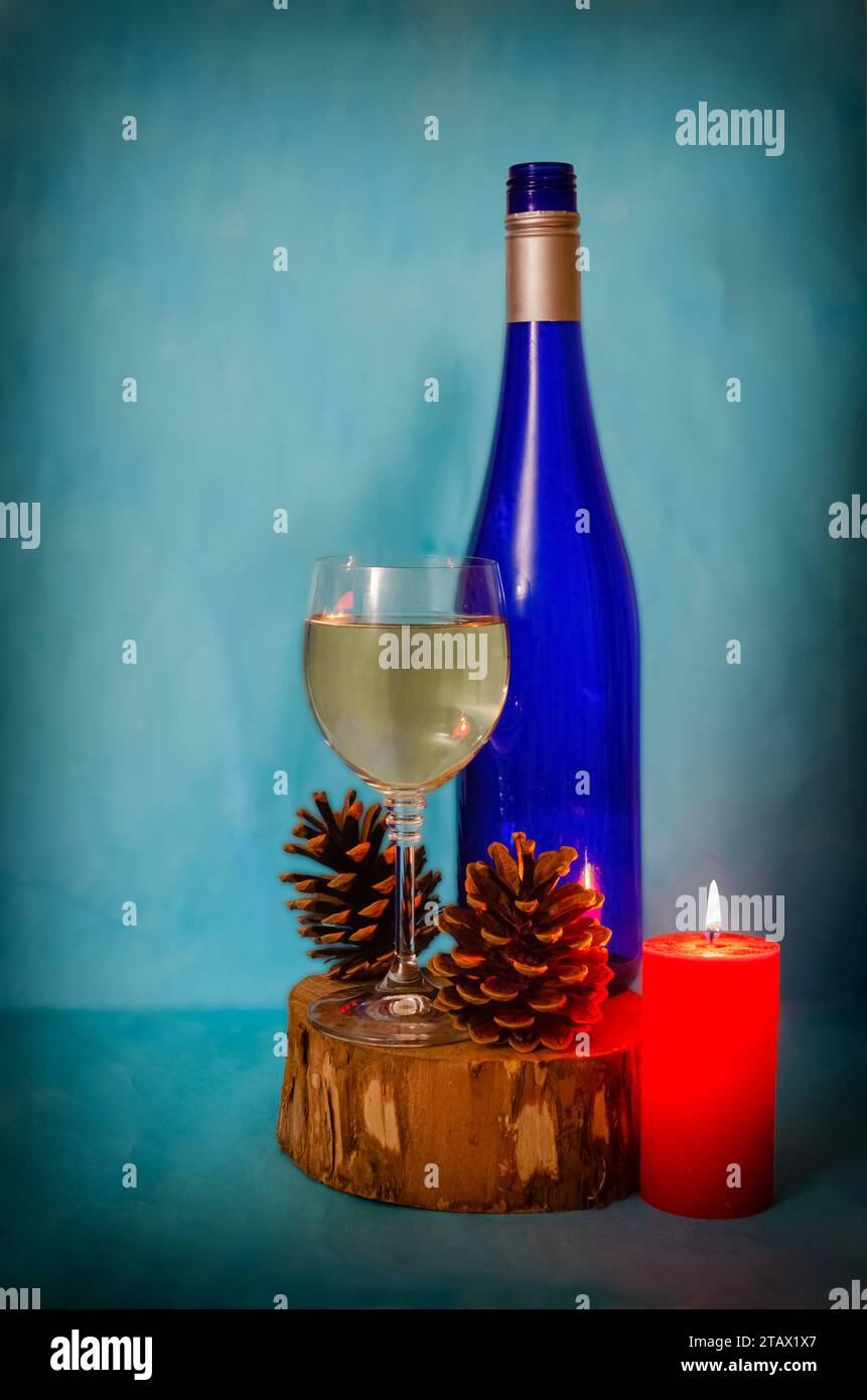 Nahaufnahme einer Weinflasche, eines Glases und einer roten Kerze auf einem Holzstumpf. Blaue Flasche, gemalter Papierhintergrund Stockfoto
