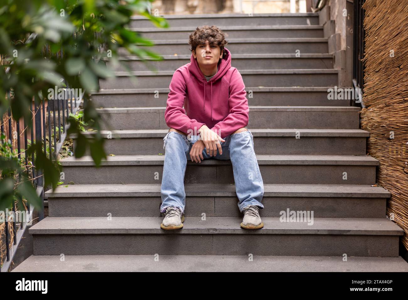 Entspannter Teenager, der draußen auf Treppen sitzt und die urbane Umgebung in lässiger Streetwear genießt Stockfoto