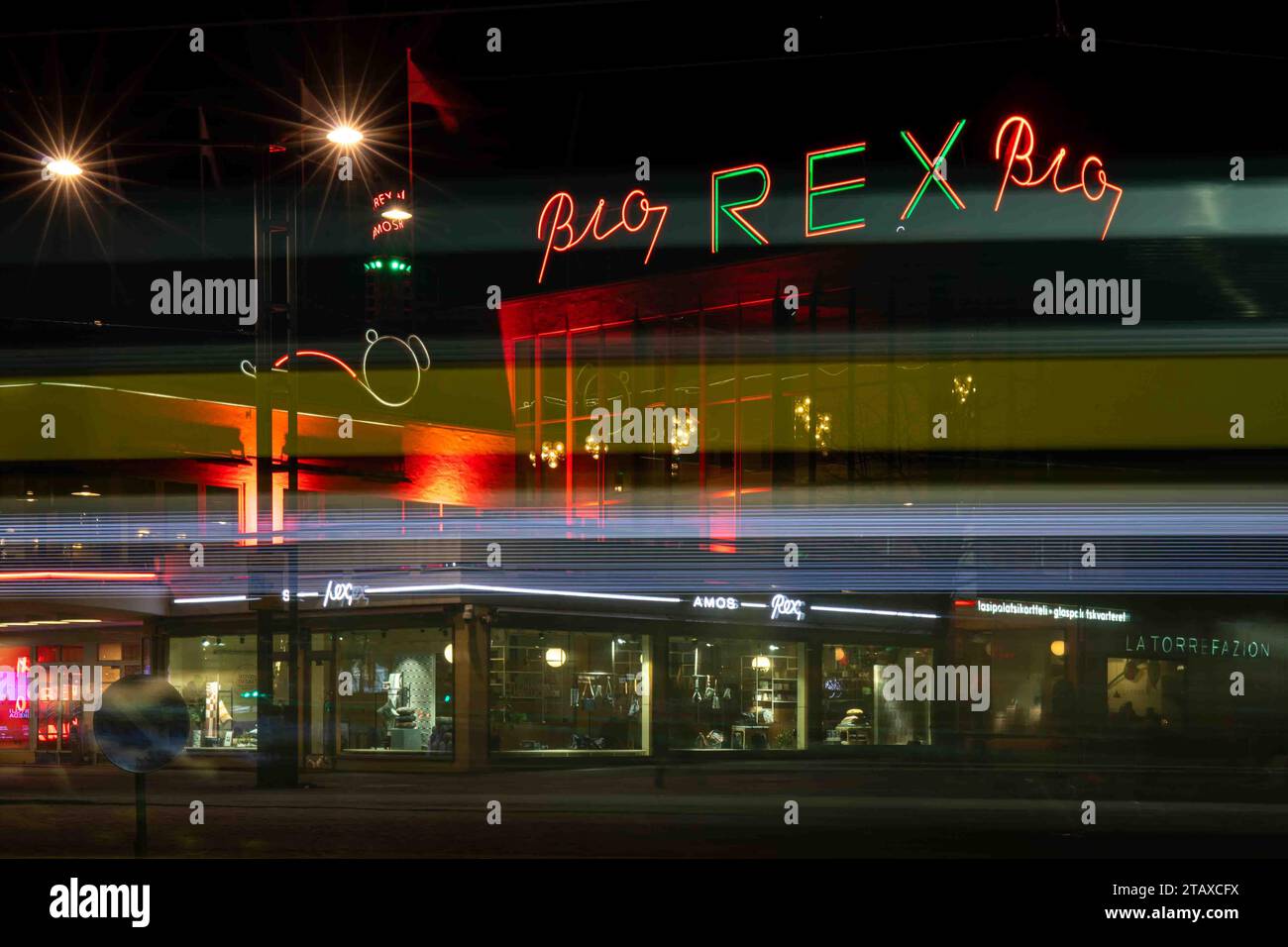 Verschwommene Bewegung einer Straßenbahn, die am Lasipalatsi-Gebäude mit Bio Rex-Neonlichtern im Kamppi-Viertel in Helsinki, Finnland, vorbeifährt Stockfoto