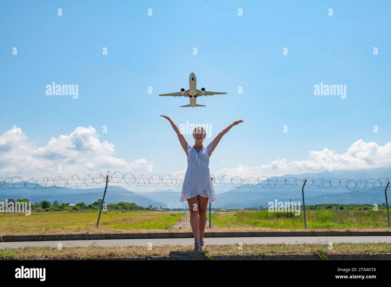 Ein Mädchen in einem weißen Kleid steht auf der Straße und streckt ihre Hände am Himmel zum Flugzeug Stockfoto