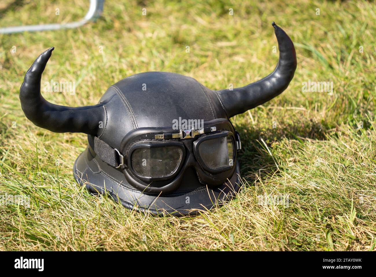 Motorradhelm aus schwarzem Leder mit Brille und Teufelshörnern im Gras Stockfoto