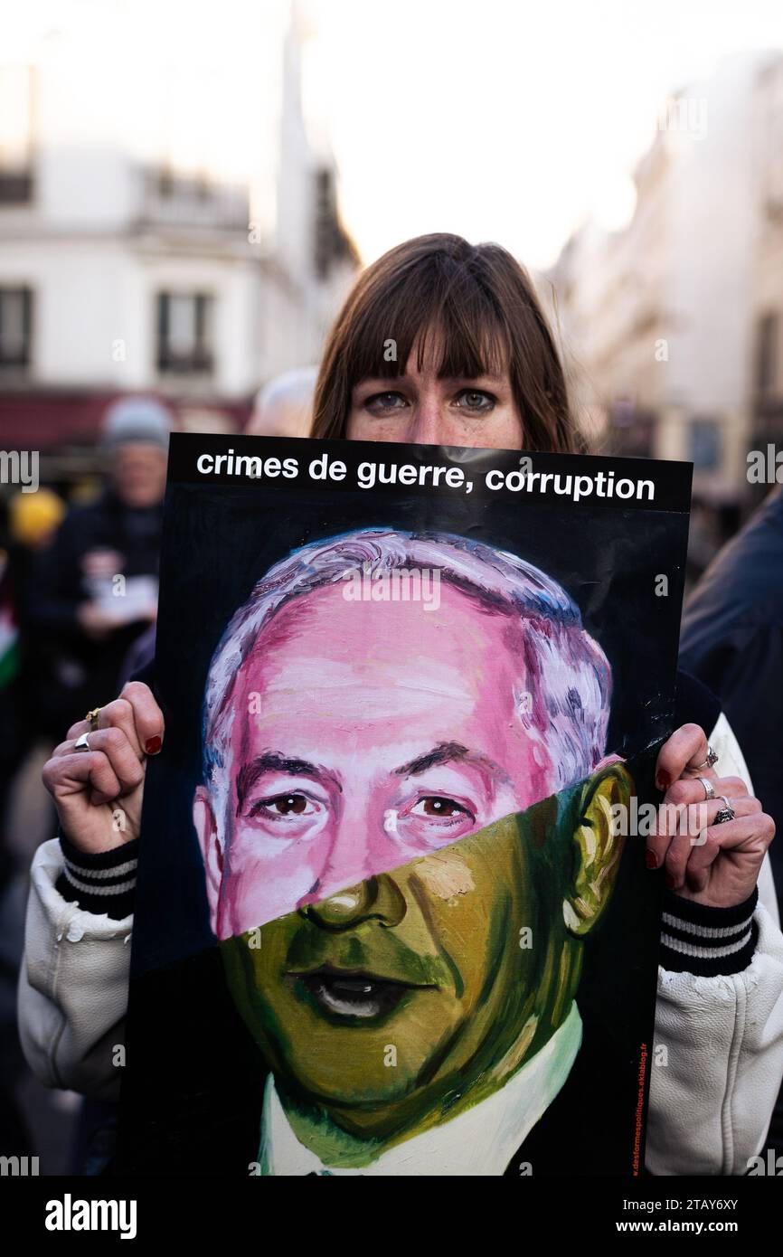 Paris, Frankreich. Dezember 2023. Eine Frau hält ein Plakat mit dem Bild des israelischen Premierministers Benjamin Netanjahu, auf dem während der Friedensdemonstration in Gaza "Kriegsverbrechen, Korruption" steht. In Paris kamen mehrere linke Organisationen und die Partei La France Insoumise zusammen, um einen sofortigen Waffenstillstand des israelischen Staates zu fordern und beschuldigten den französischen Präsidenten Emmanuel Macron, an den Massakern in Gaza beteiligt zu sein. Die Demonstration begann am Place de Republique und endete am Place Bastille. (Foto: Telmo Pinto/SOPA Images/SIPA USA) Credit: SIPA USA/Alamy Live News Stockfoto