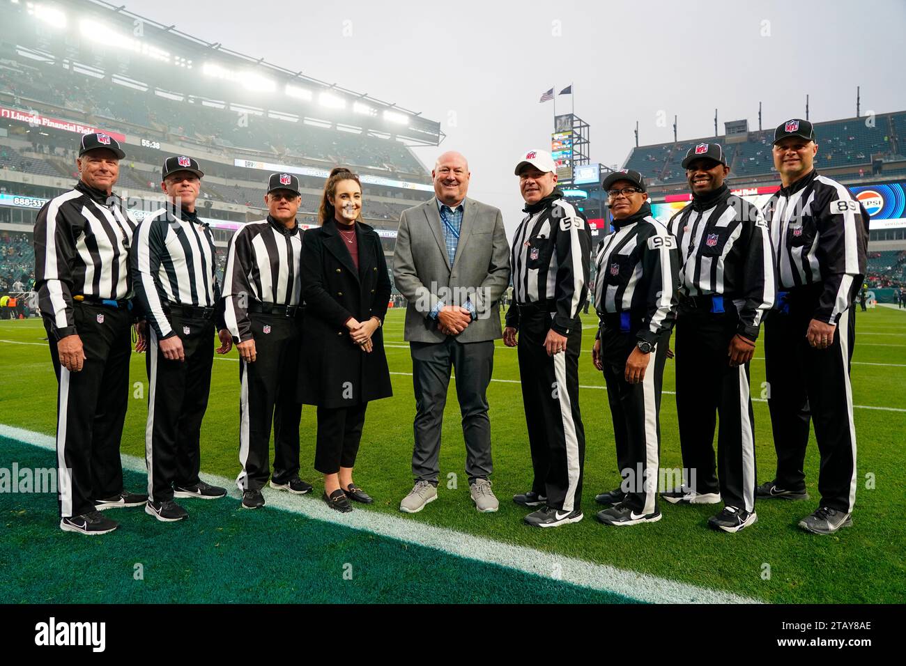 The officiating crew, from left, back judge Scott Helverson (93), down judge Danny Short (113), line judge Rusty Baynes (59), referee Alex Kemp (55), field judge James Coleman (95), field judge Sean Petty (28) and umpire Mike Morton pose in uniform with replay officials Jamie Alfieri Tuss, center left, and Mike Chase, center right, prior to an NFL football game between the Philadelphia Eagles and the San Francisco 49ers, Sunday, Dec. 3, 2023, in Philadelphia. (AP Photo/Chris Szagola) Stockfoto
