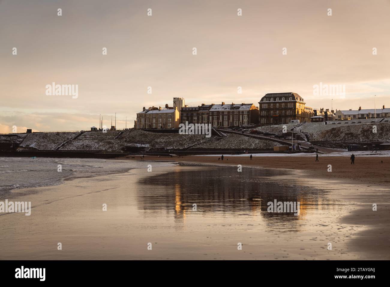 Reflexion des Grand Hotels in Tynemouth über den nassen Sand von Longsands Beach bei Sonnenuntergang im Dezember mit Schnee am Strand Stockfoto