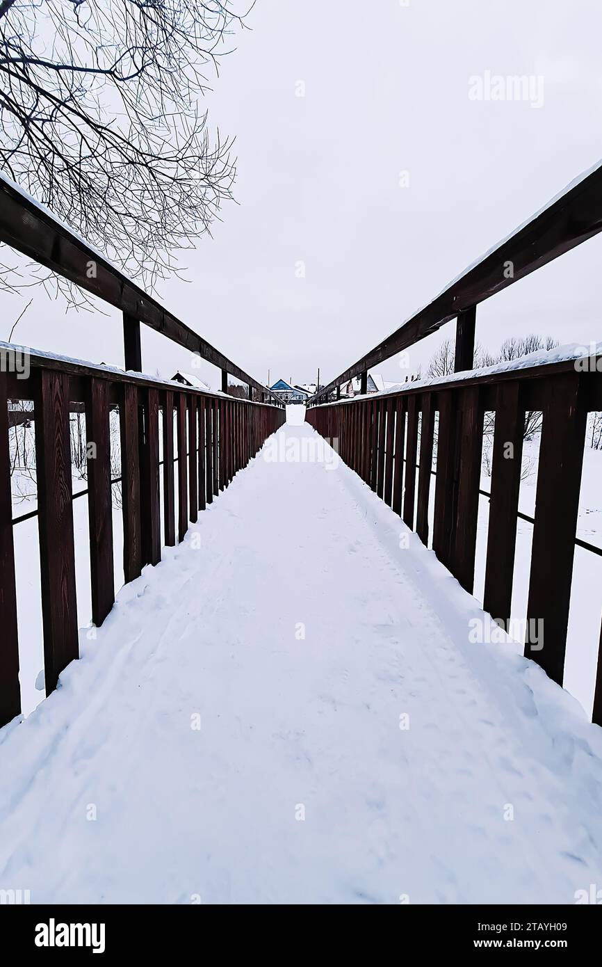 Schneebedeckte Holzbrücke im Park am Wintertag. Fußgängerbrücke mit Schnee bedeckt. Perspektive Stockfoto