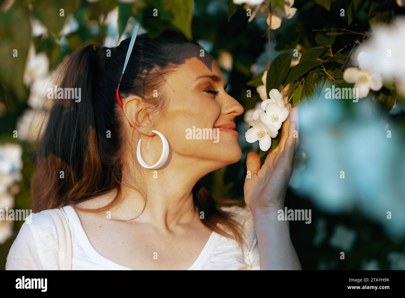 Sommerzeit. Glückliche elegante Frau in weißem Hemd in der Nähe des blühenden Baumes. Stockfoto