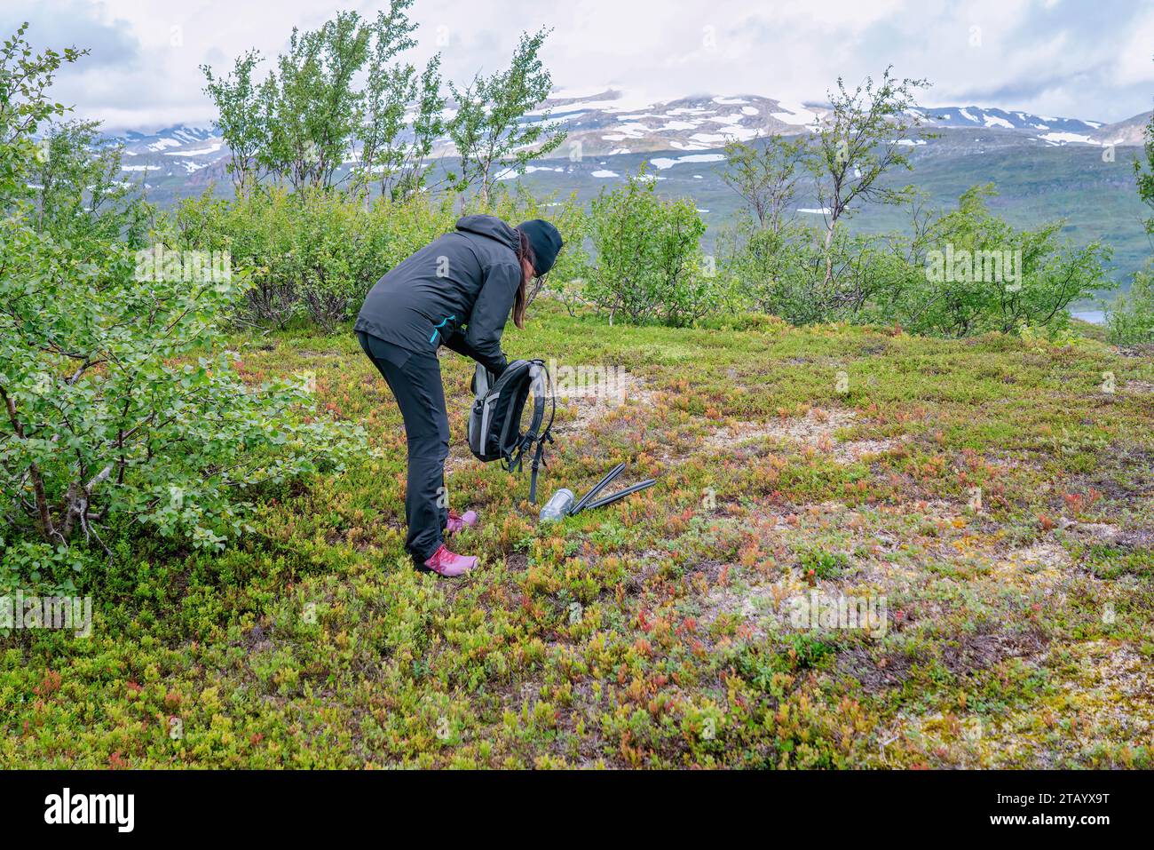 Reife Frau macht eine Pause und entlädt Dinge aus dem Rucksack für eine Ruhepause, wandert hoch in den norwegischen Bergen. Gesunder Lebensstil. Norwegen, Krutvatnet Stockfoto