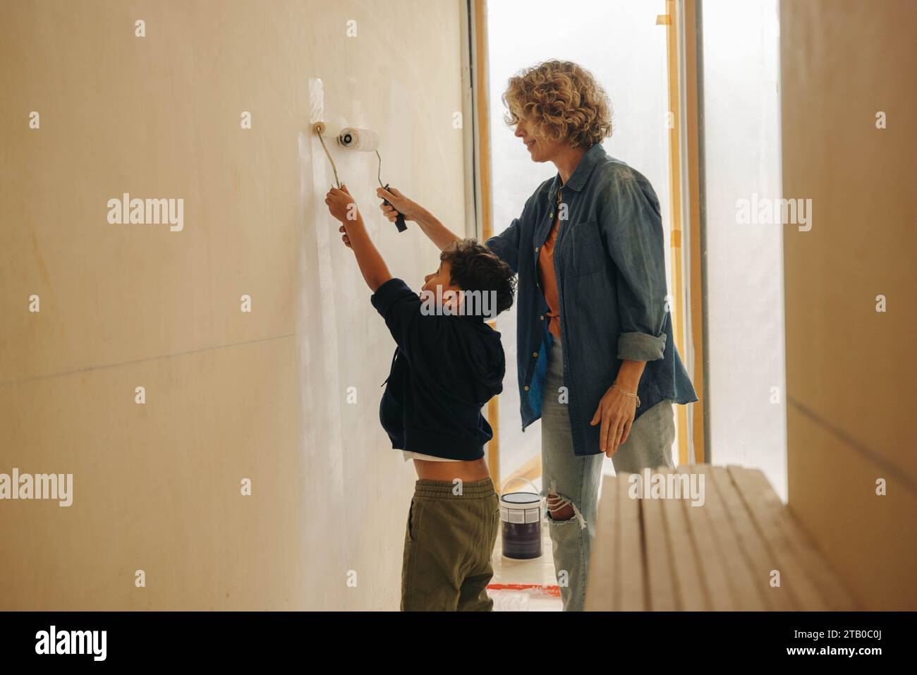 Heimwerkerarbeit zu Hause mit einer kaukasischen Mutter und ihrem jungen Sohn, die zusammen eine Innenwand malen. Mutter und Kind, die eine Hausrenovierung durchführen und das Stockfoto
