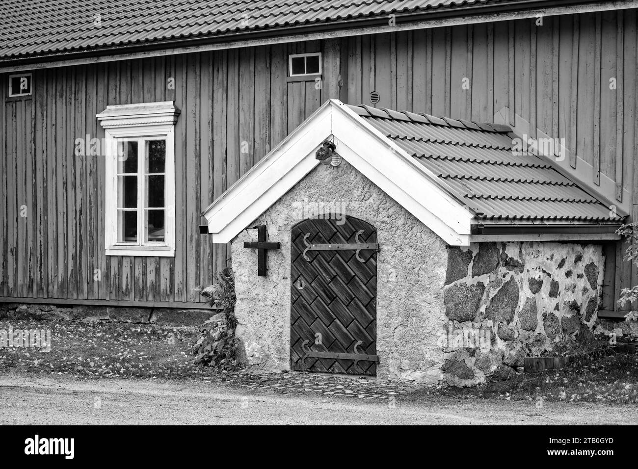 Eingang zum alten Leichenkeller mit verschlossener Tür und Kreuz. Schwarzweißkonvertierung. Muurla, Finnland. Stockfoto