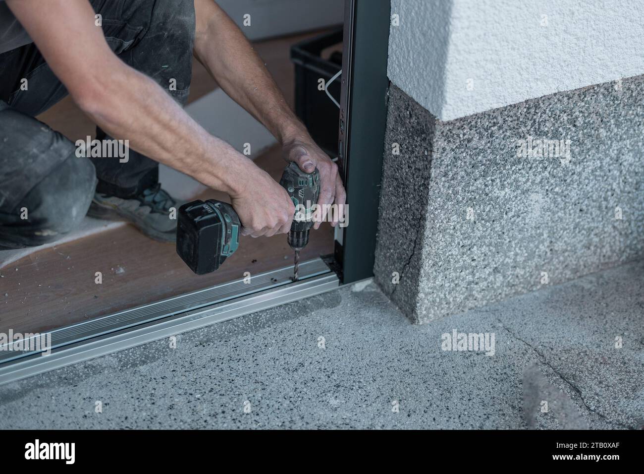 Jemand bohrt die Schwelle einer Tür heraus, damit sie sich auf den Boden verschraubt. Details zur Installation der Eingangstür, moderne Tür in einem alten Haus. Stockfoto