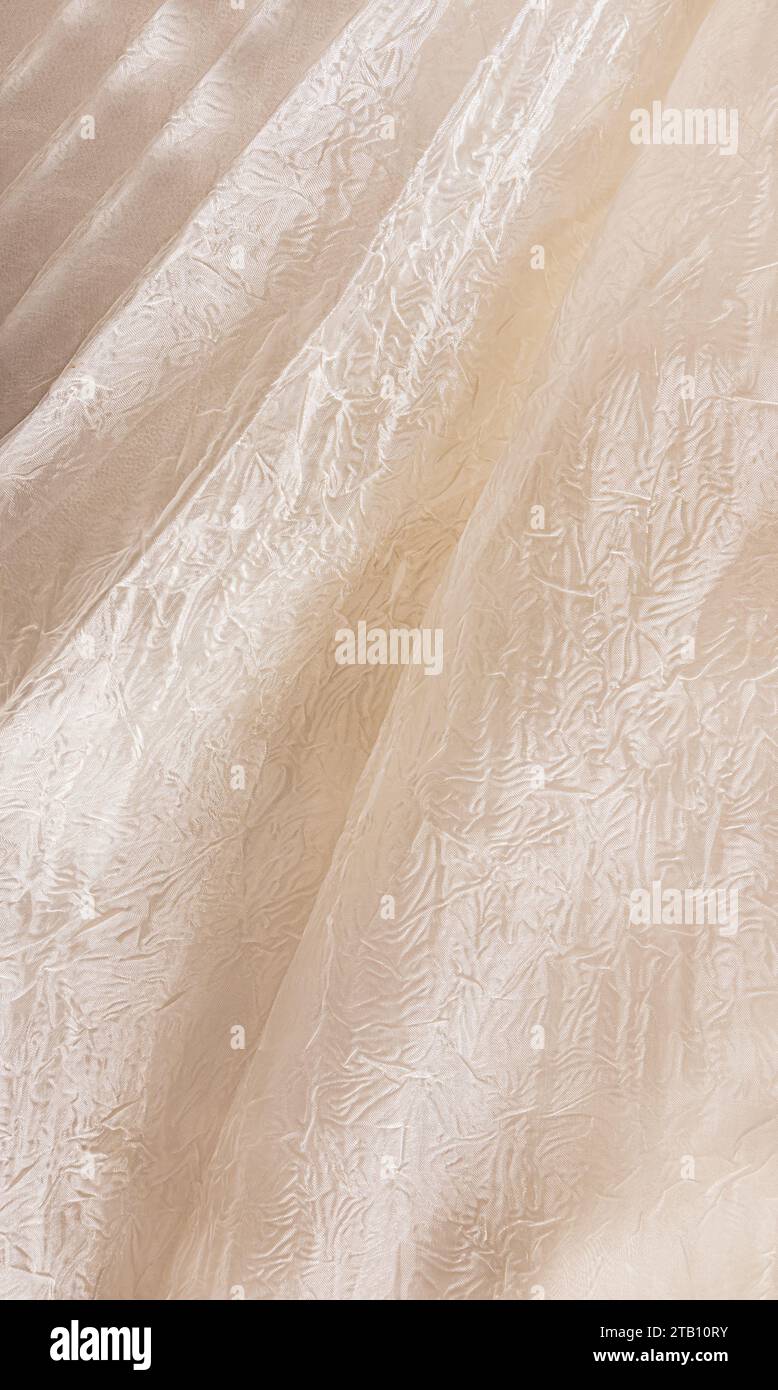 Vertikale Ansicht von schicken weichen Falten aus Fabrikgewebe mit Verzierung. Beige, Champagnerfarbe, Elfenbein, cremig. Abstrakter Hintergrund aus Hochzeitsstoff Stockfoto
