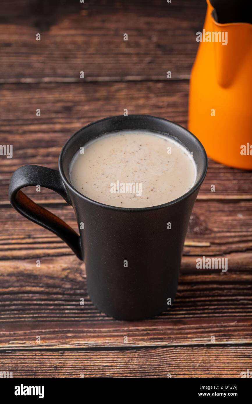 Milch mit türkischem Kaffee in schwarzer Tasse auf Holztisch Stockfoto