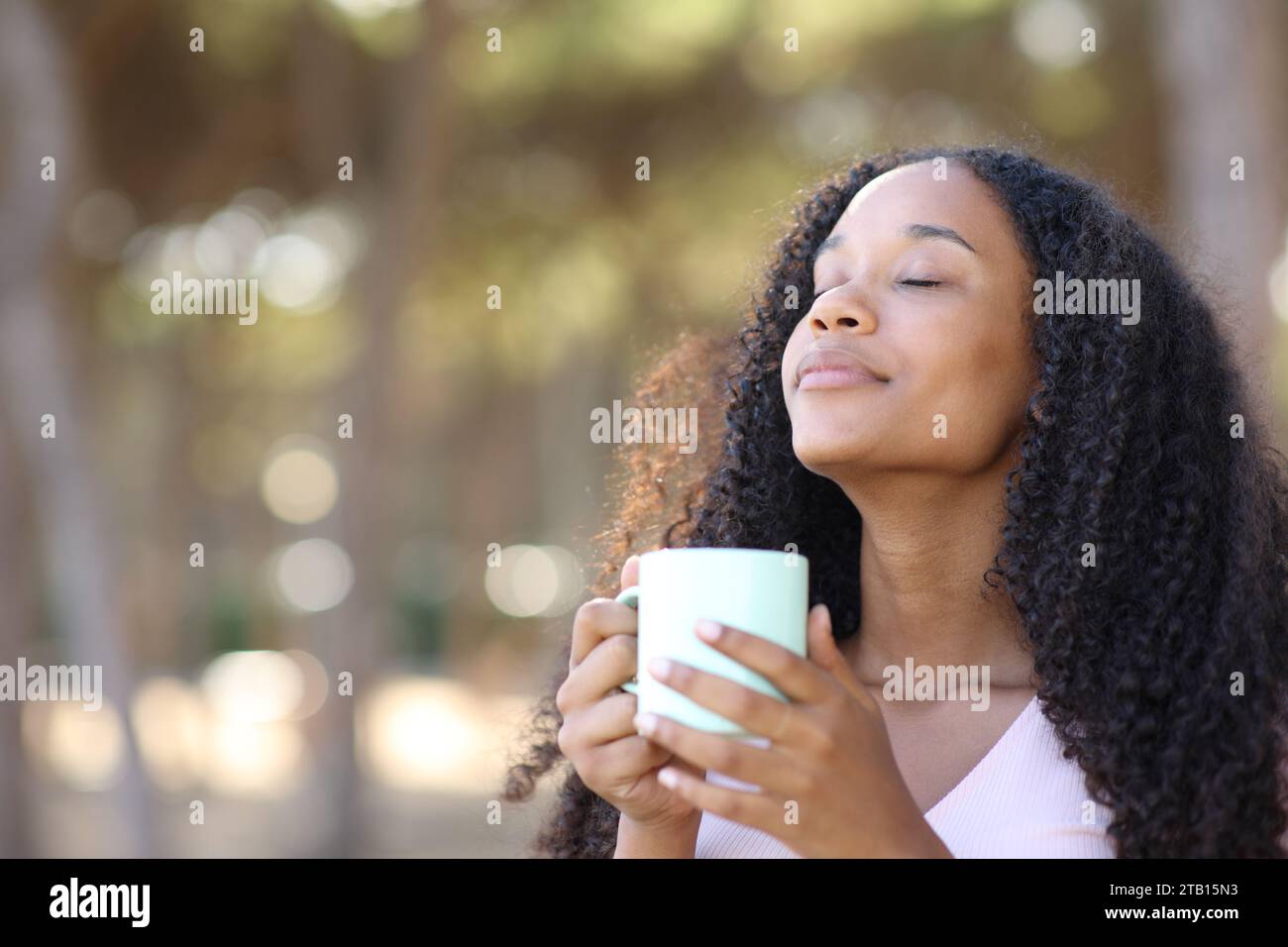 Schwarze Frau riecht Kaffee aus einer Tasse, die im Park steht Stockfoto
