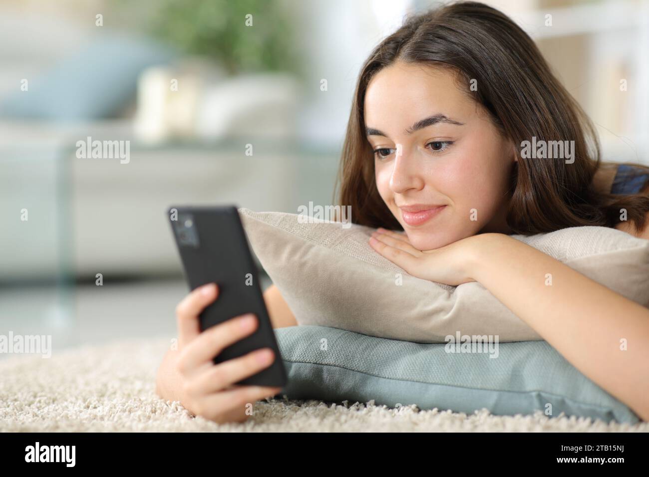 Zufriedene Frau, die zu Hause auf dem Boden liegende Telefoninhalte ansieht Stockfoto