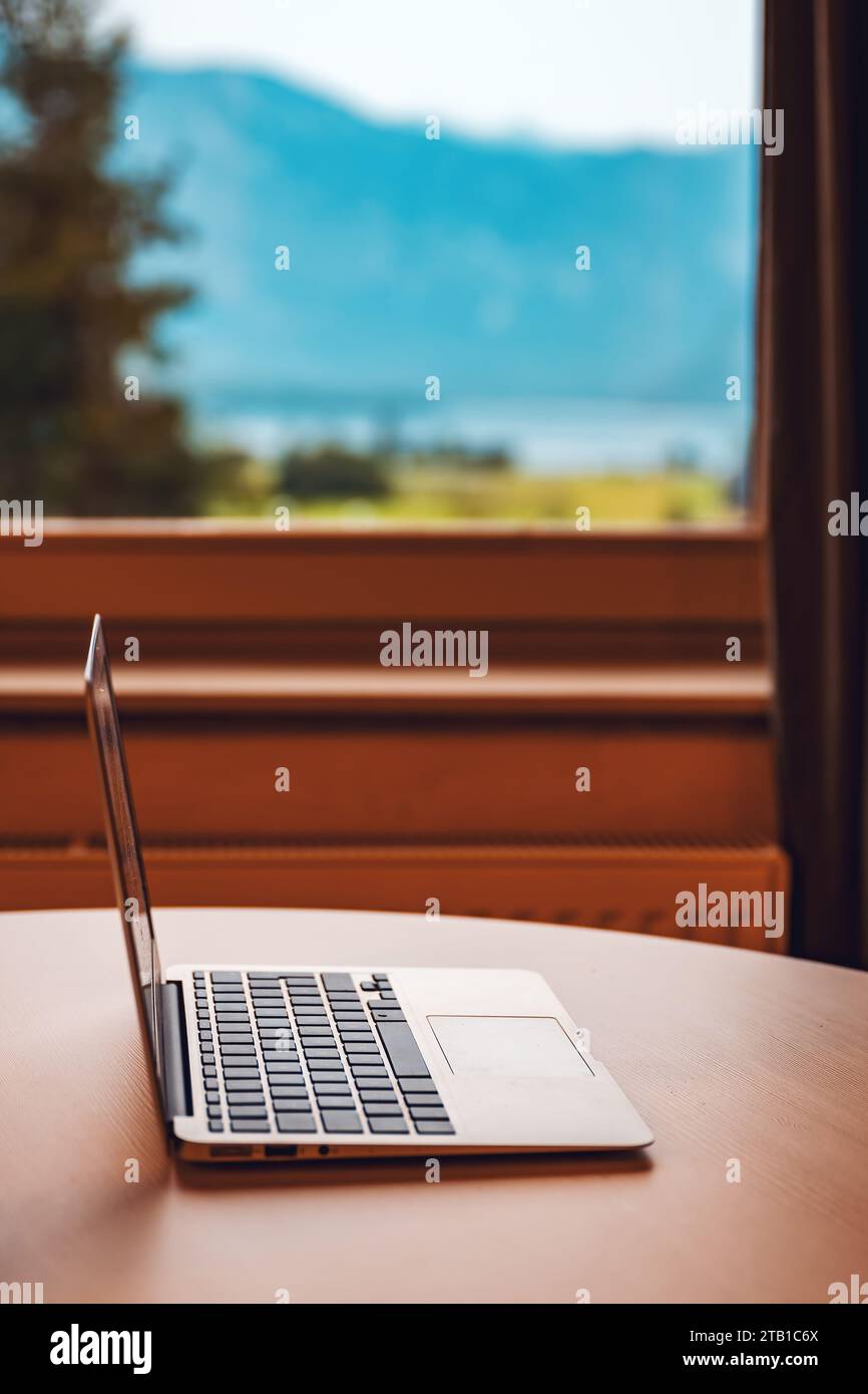 Laptop-Computer auf Wohnzimmer Schreibtisch am Fenster mit wunderschönem Blick auf die Sommerlandschaft, selektiver Fokus Stockfoto