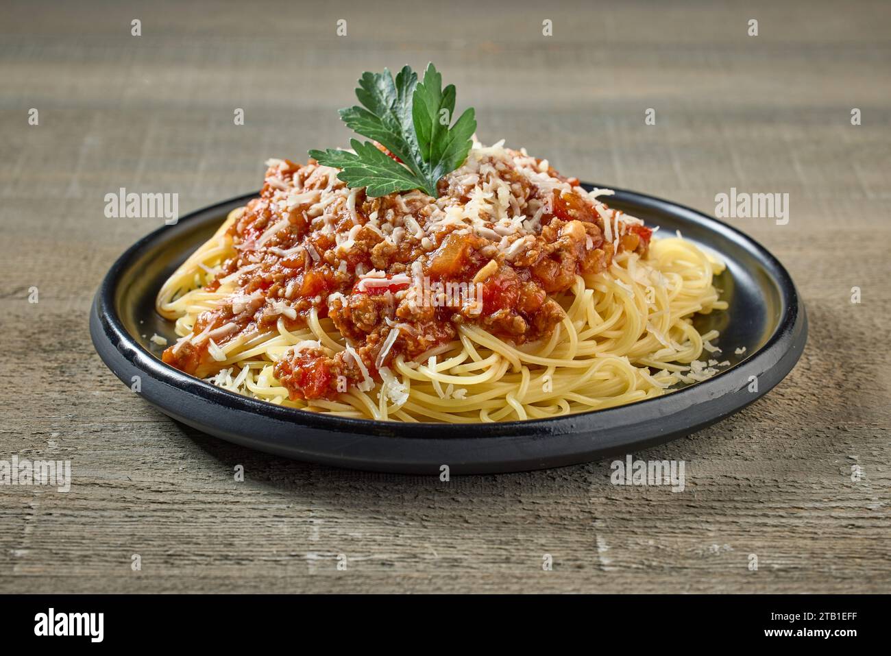 Spaghetti mit Soße Bolognese auf schwarzem Teller auf hölzernem Küchentisch Stockfoto