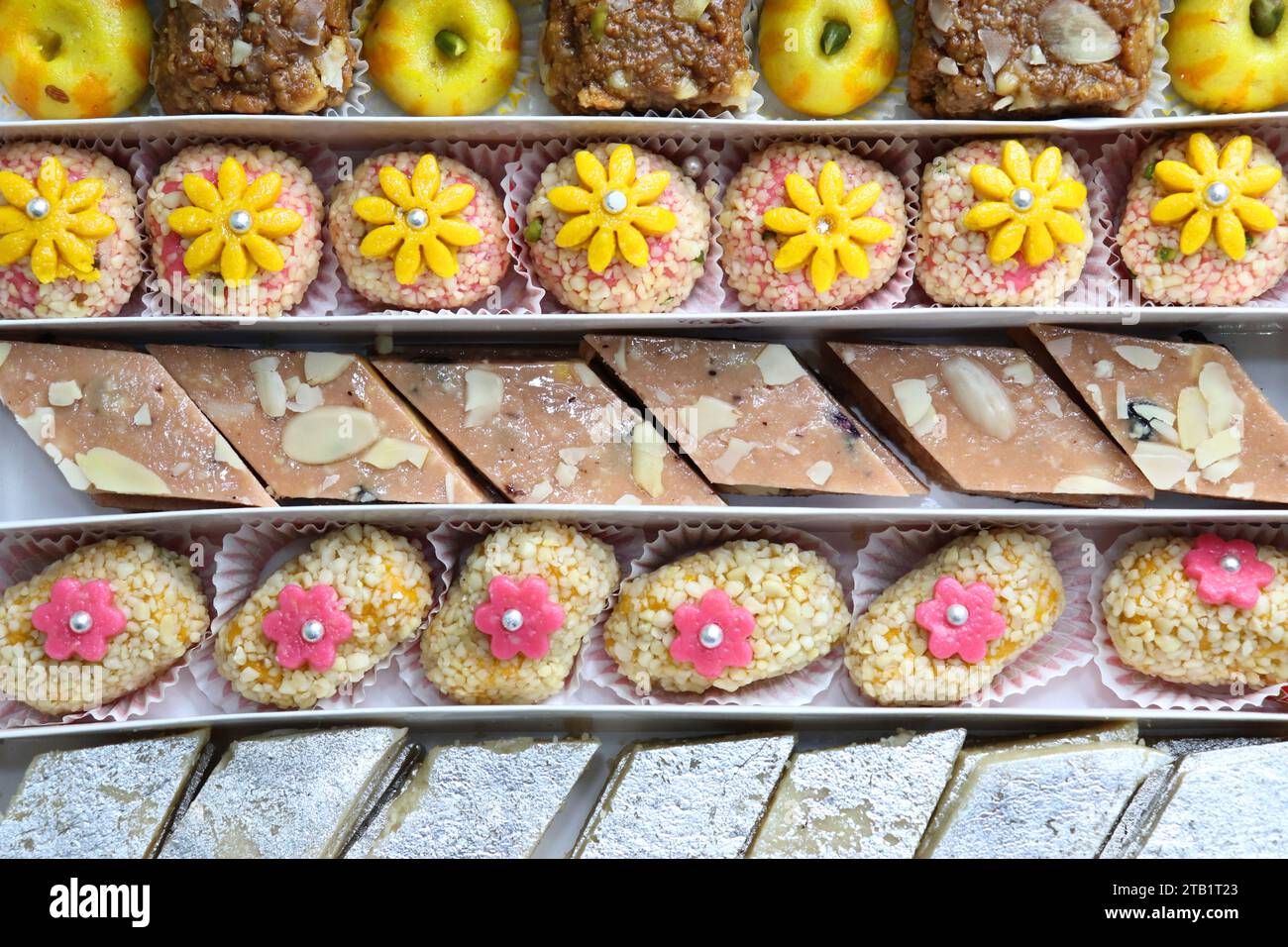 Indische Diwali-Süßigkeiten oder Mithai mit Diya und Blumen. Festliche Geschenkidee. Kaju Katli, Trockenfrüchte Peda, Barfi, Cashewnuss Barfi, Marzipans. Stockfoto