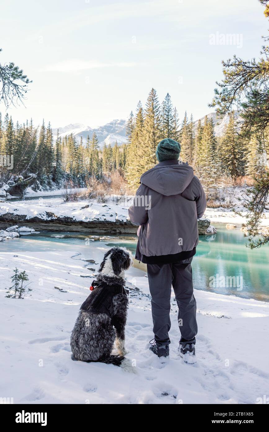 Mann auf Winterwanderung mit Hund entlang des Gebirgsflusses in Canmore, Alberta Stockfoto