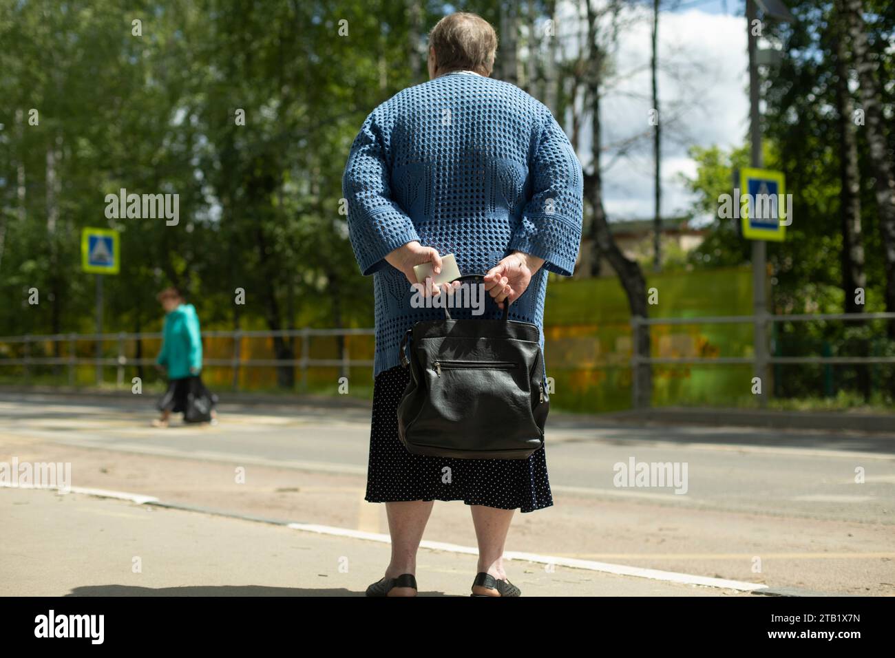 Der Rentner wartet auf den Bus auf der Straße. Oma mit Tasche. Stockfoto