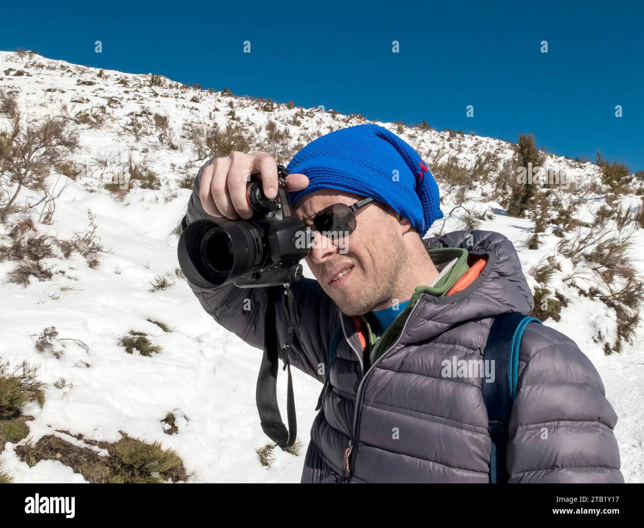 Mann in einer Wollmütze, der Fotos auf einem schneebedeckten Berg macht Stockfoto