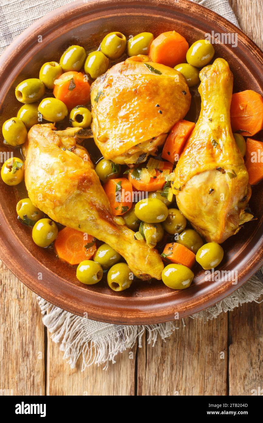 Tajine Zitoune ist ein algerisches Eintopfgericht, das aus Hühnchen besteht, das mit Karotten und grünen Oliven gekocht wird, wobei nordafrikanische Gewürze aus nächster Nähe auf hölzernem ta verwendet werden Stockfoto
