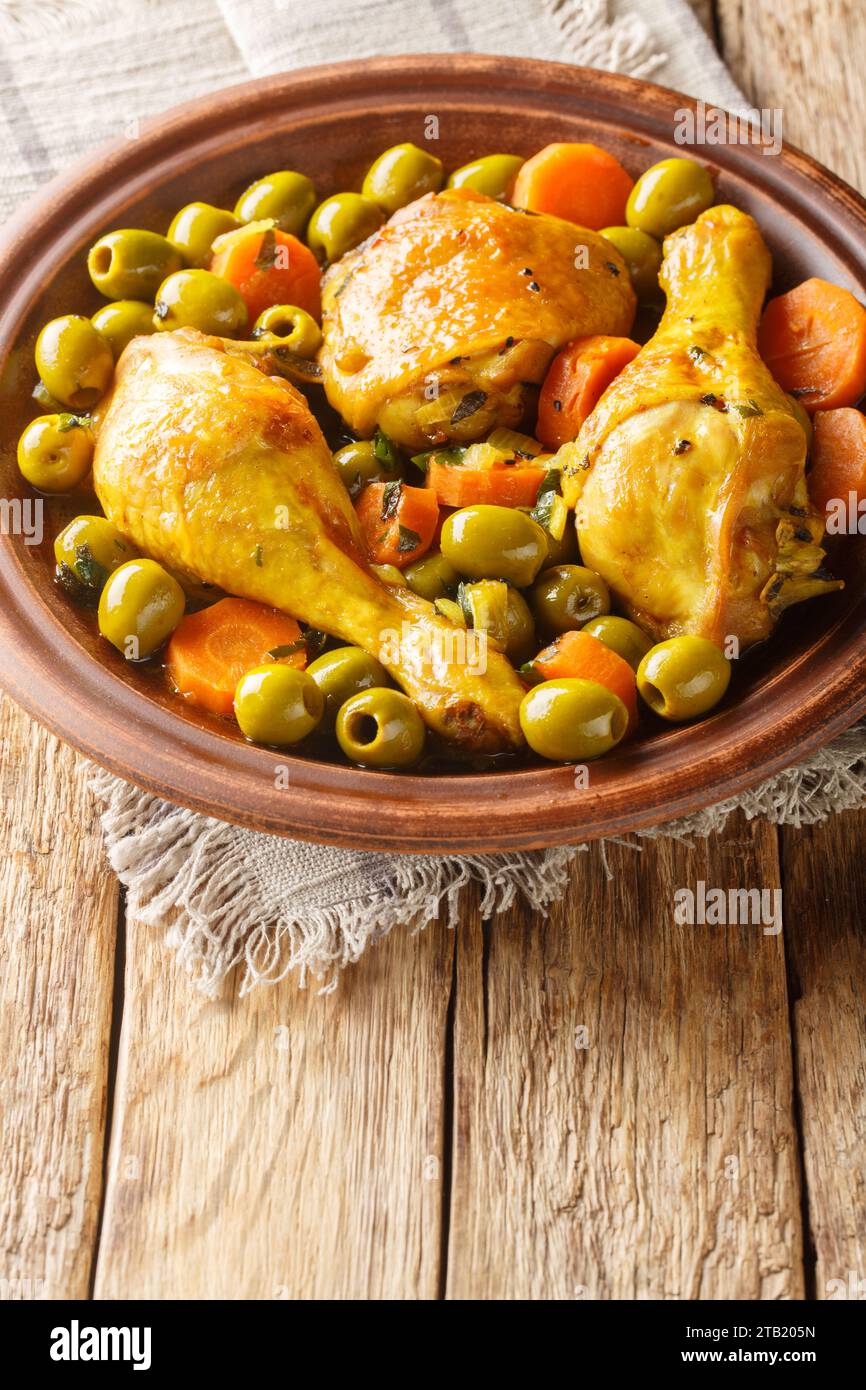 Tajine Zitoune ist ein algerisches Eintopfgericht, das aus Hühnchen besteht, das mit Karotten und grünen Oliven gekocht wird, wobei nordafrikanische Gewürze aus nächster Nähe auf hölzernem ta verwendet werden Stockfoto