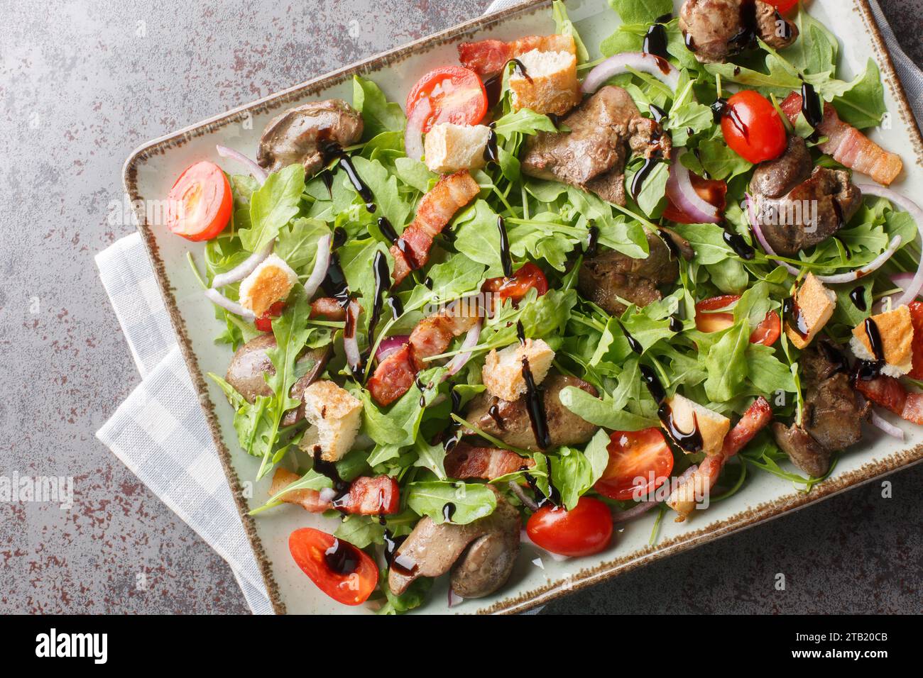 Gesunde Salatvorspeise aus gebratener Hühnerleber, Rucola, Zwiebeln, Tomaten, Croutons und Speck Nahaufnahme in einem Teller auf einem Tisch. Horizontale Draufsicht von Stockfoto