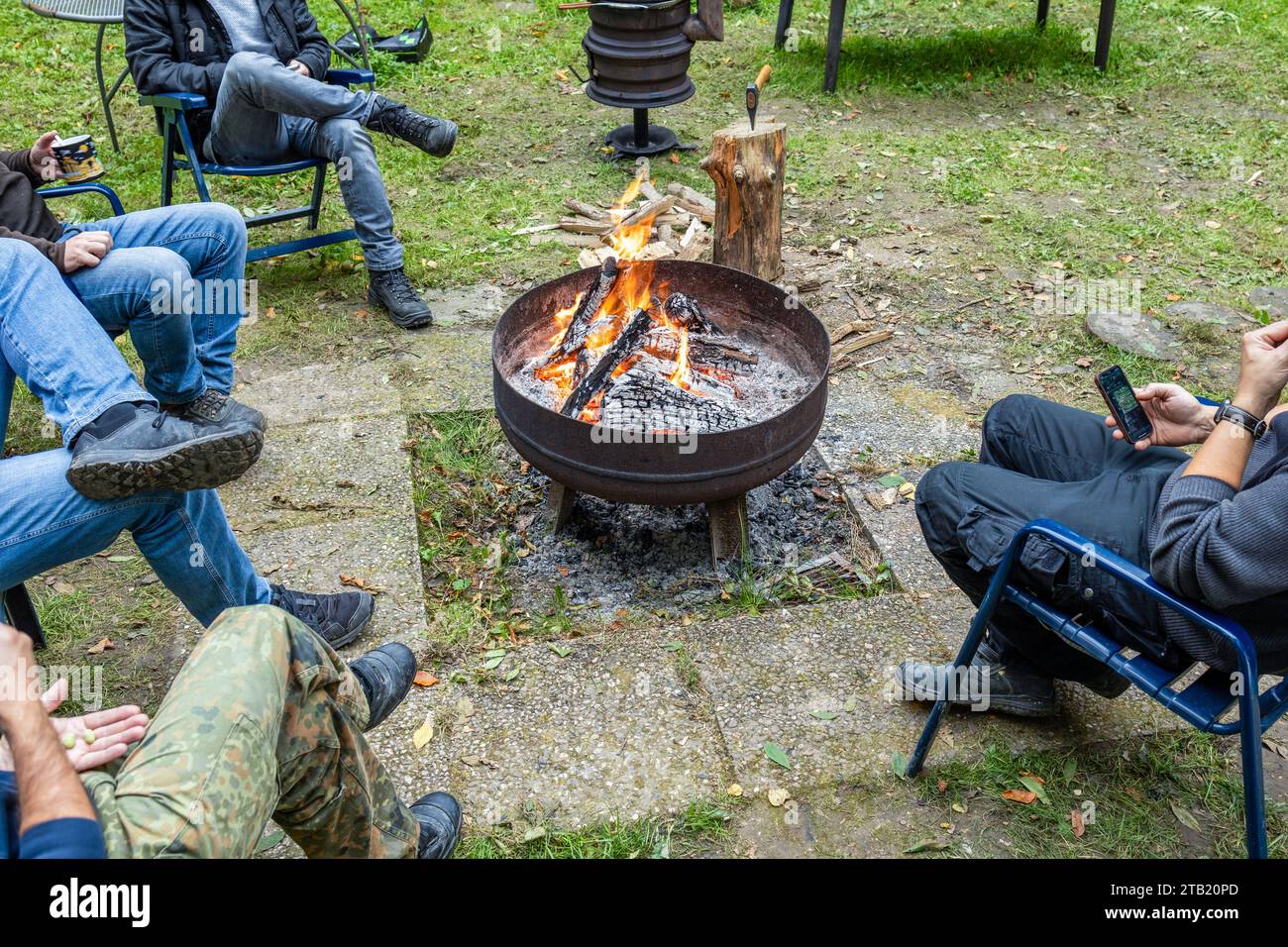 Männer sitzen im Kreis unter freiem Himmel in der Nähe der Feuerschüssel Stockfoto