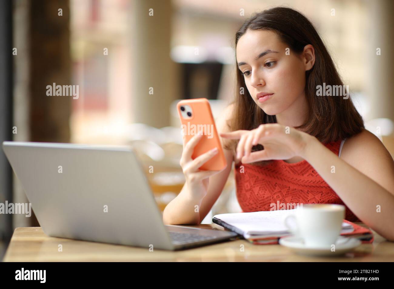 Ernsthafte Frau, die Telefon und Laptop auf einer Bar-Terrasse überprüft Stockfoto