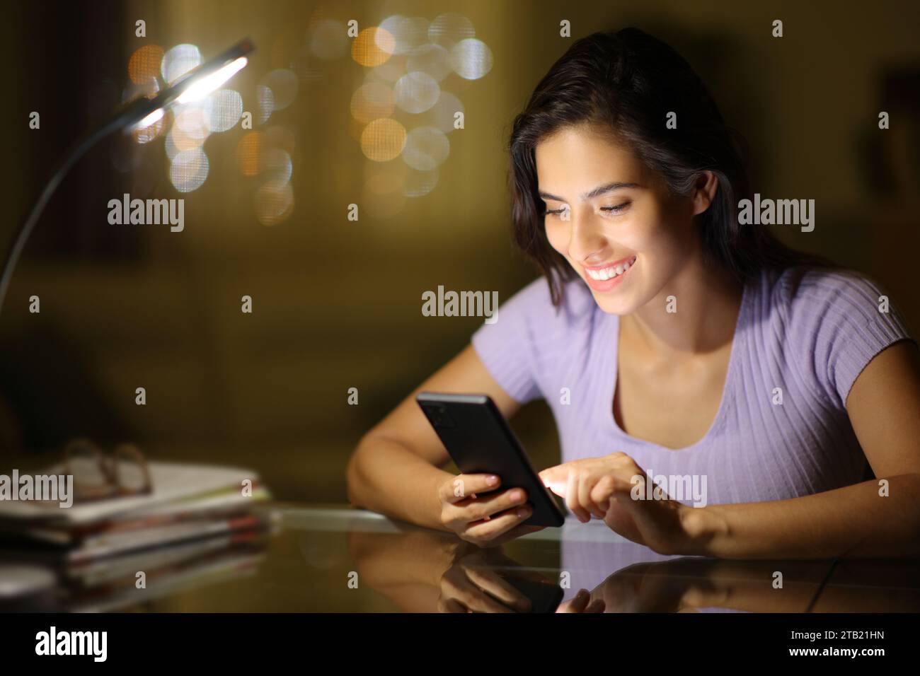 Glückliche Frau in der Nacht, die ihr Handy zu Hause benutzt Stockfoto