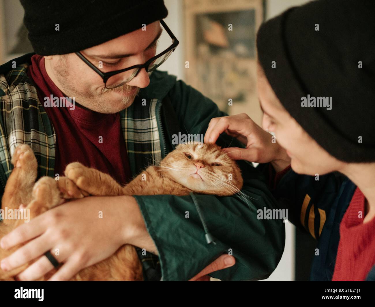 Gemütliches Paar in Mützen, hält und streichelt ein orangenes schottisches F Stockfoto