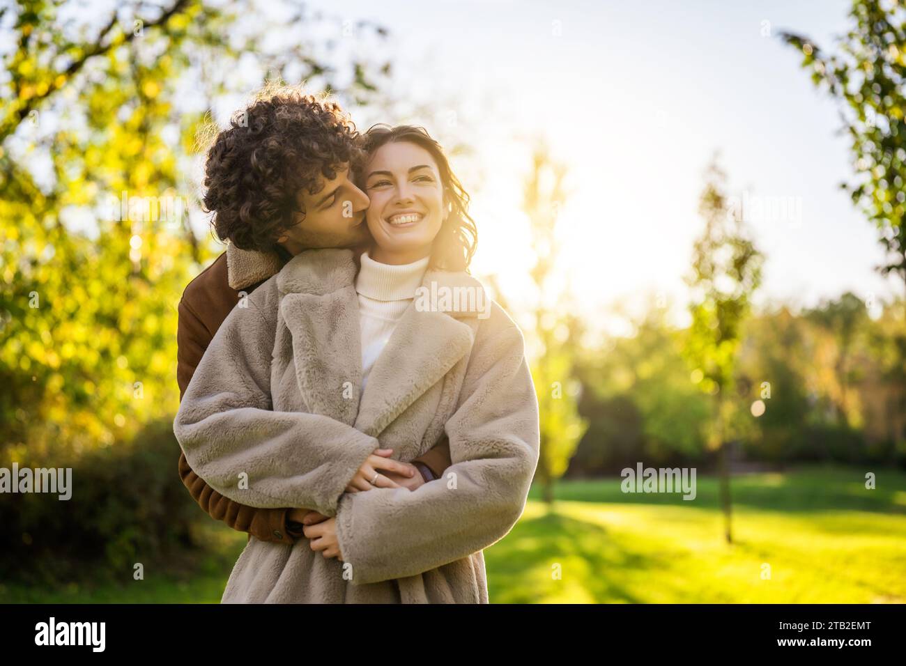 Glückliches, liebevolles Paar, das sich bei Sonnenuntergang im Park umschließt und küsst. Stockfoto