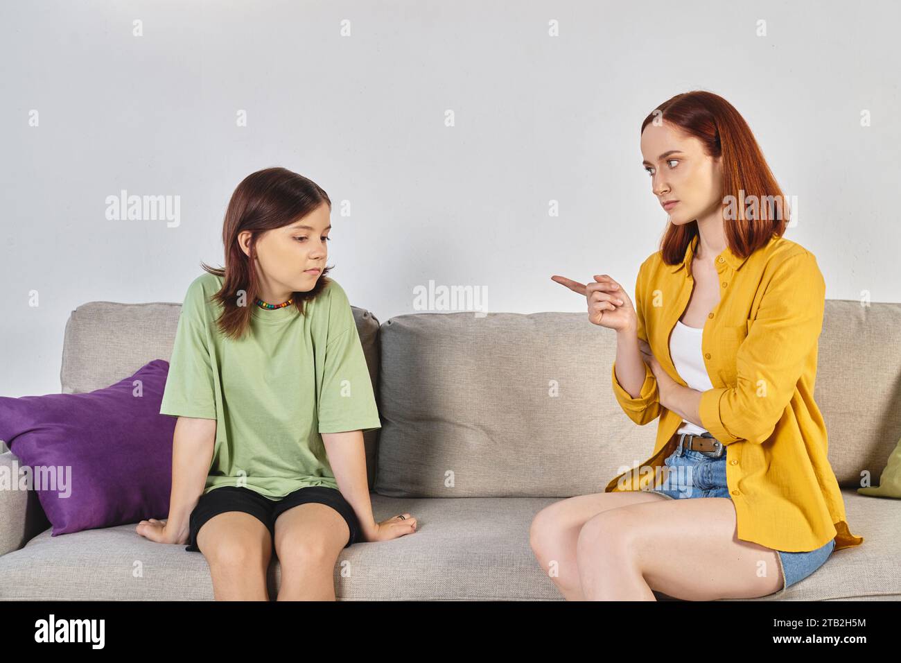 Ernsthaftes Gespräch, strenge Mutter zeigt auf frustrierte Teenager-Tochter, die im Wohnzimmer auf der Couch sitzt Stockfoto