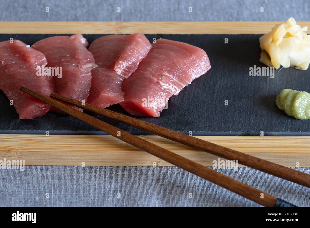Japanisches Hausessen - hausgemachte rohe Akami-Thunfisch-Sashimi auf einem Schieferbrett mit Holzstäbchen, Ingwer und Wasabi. UK Stockfoto
