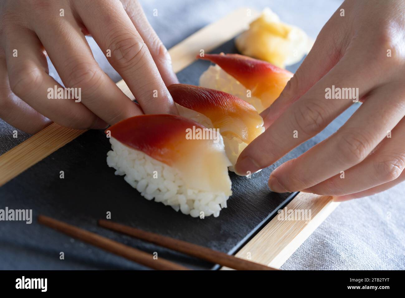 Asiatische Frau, die ein Stück hochwertiges Surfmuschel-Sushi (Japanisch: Hokkigai oder Ubaggai) auf ein Schieferbrett legt. Hausgemachte japanische Gerichte Stockfoto