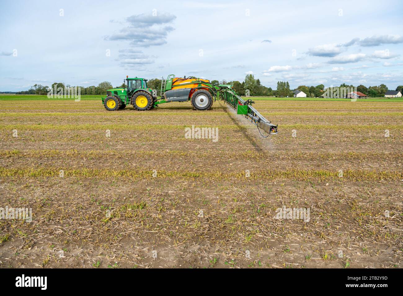 Spurenelemente auf einem neu gesäten Rapsfeld ausbreiten. John Deere 6620 Traktor und gezogene Feldspritze Amazone UX 4201 Stockfoto