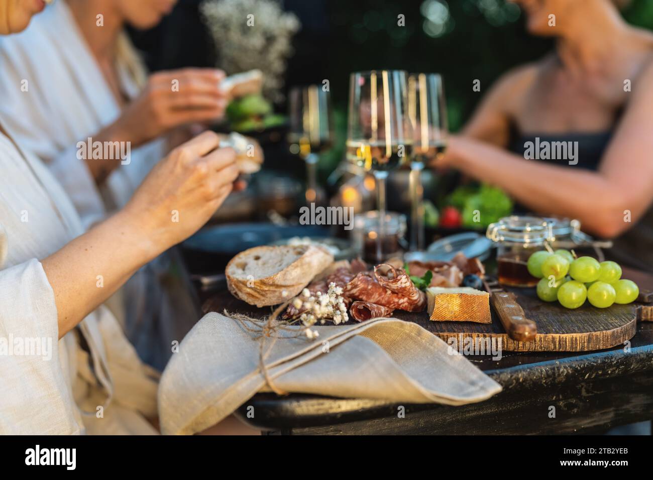 Nahaufnahme eines Tisches mit Weingläsern, Brot und Trauben, Freunde essen im Hintergrund Stockfoto