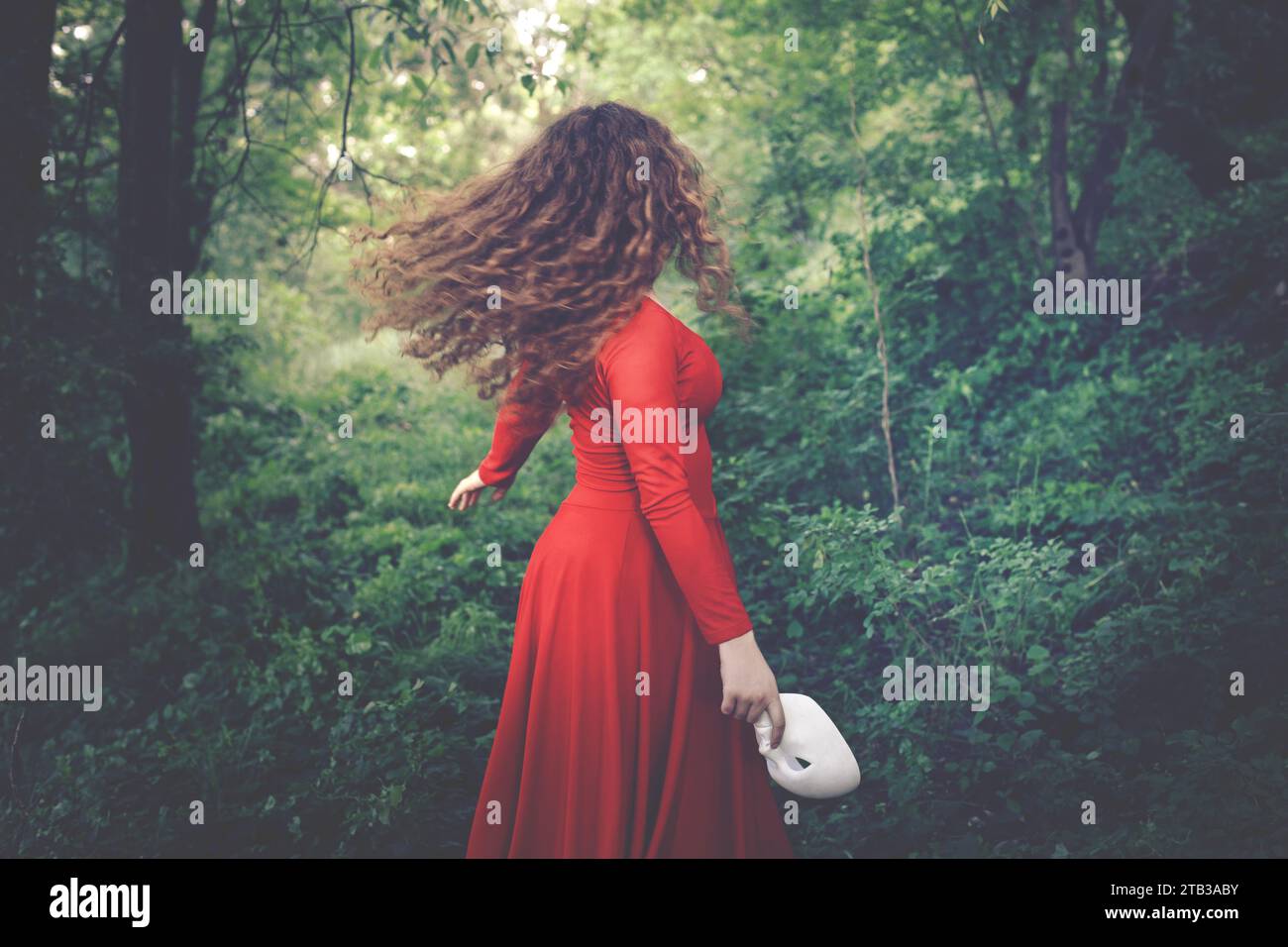 Surreale Frau in Rot gekleidet mit Maske in der Hand, die frei im Wald läuft, abstraktes Konzept Stockfoto