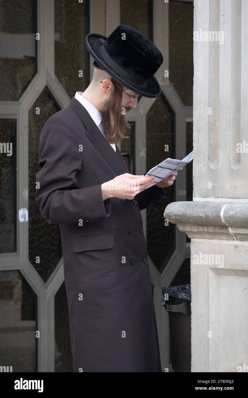 Ein orthodoxer jüdischer Mann mit langem Uncurled Peyus liest einen wöchentlichen Vorlesungskalender vor einer Satmar-Synagoge in Brooklyn, New York. Stockfoto