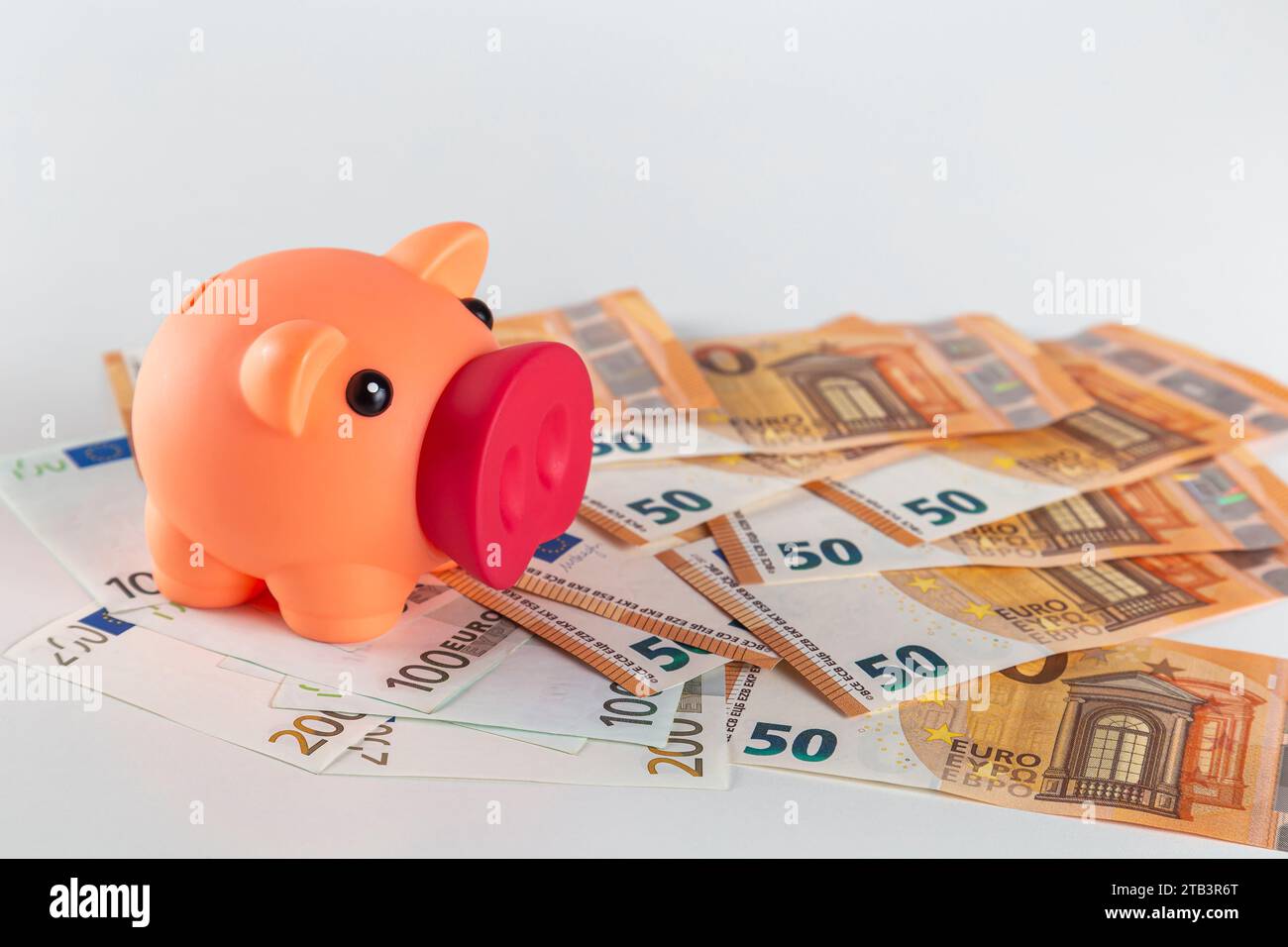 Eine pinkfarbene Schweinebank steht auf einem Tisch, der mit einer großen Menge Euro-Banknoten auf hellem Hintergrund bedeckt ist Stockfoto