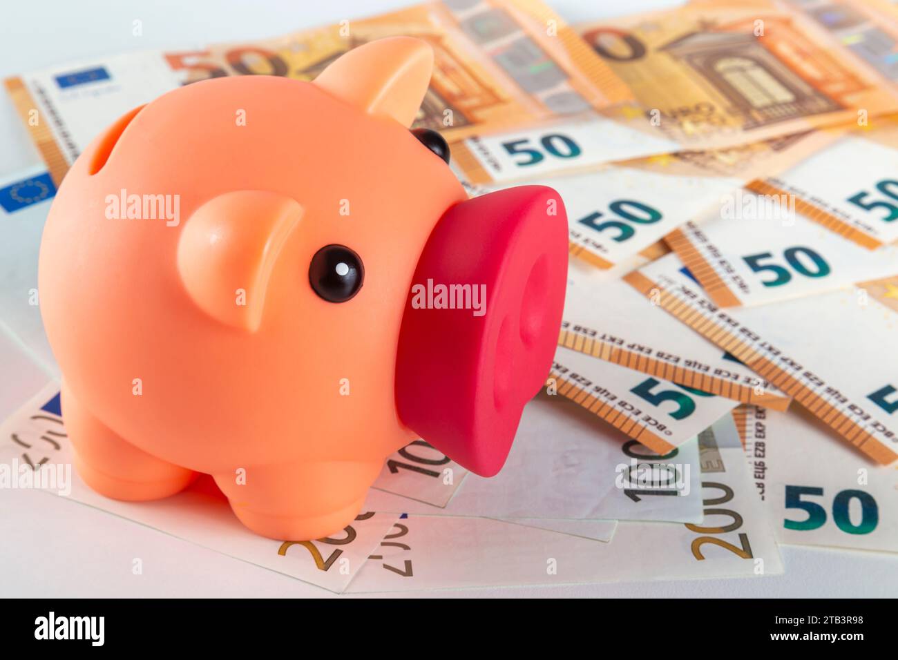 Eine pinkfarbene Schweinebank steht auf einem Tisch, der mit einer großen Menge Euro-Banknoten bedeckt ist, auf einem hellen Hintergrund in Nahaufnahme Stockfoto