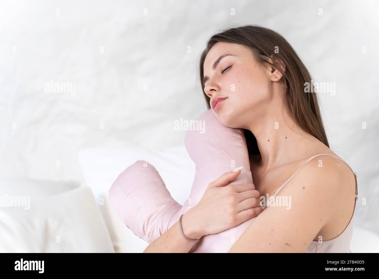 Ein süßes weißes Mädchen mit einem Schönheitskissen in den Händen sitzt im Bett und ist traurig Stockfoto