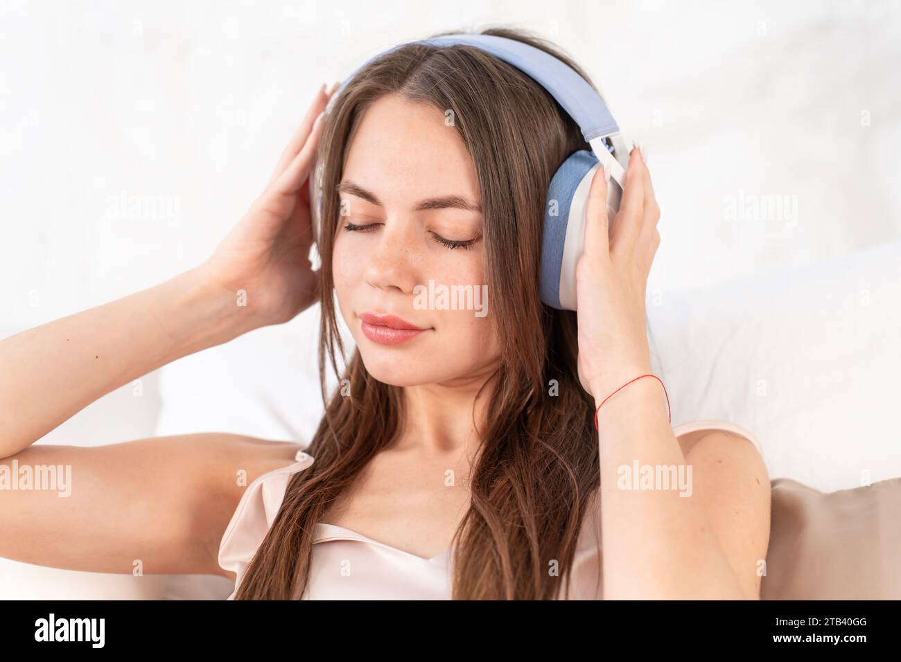 Kaukasische junge Frau mit Kopfhörern hört Musik, während sie im Bett sitzt Stockfoto