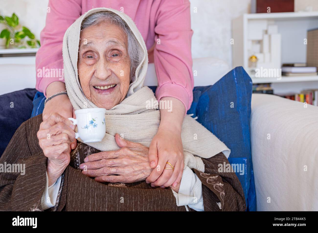 Weibliche Hände umarmen ihre Großmutter, während sie Kaffee im Wohnzimmer auf dem Sofa trinken Stockfoto