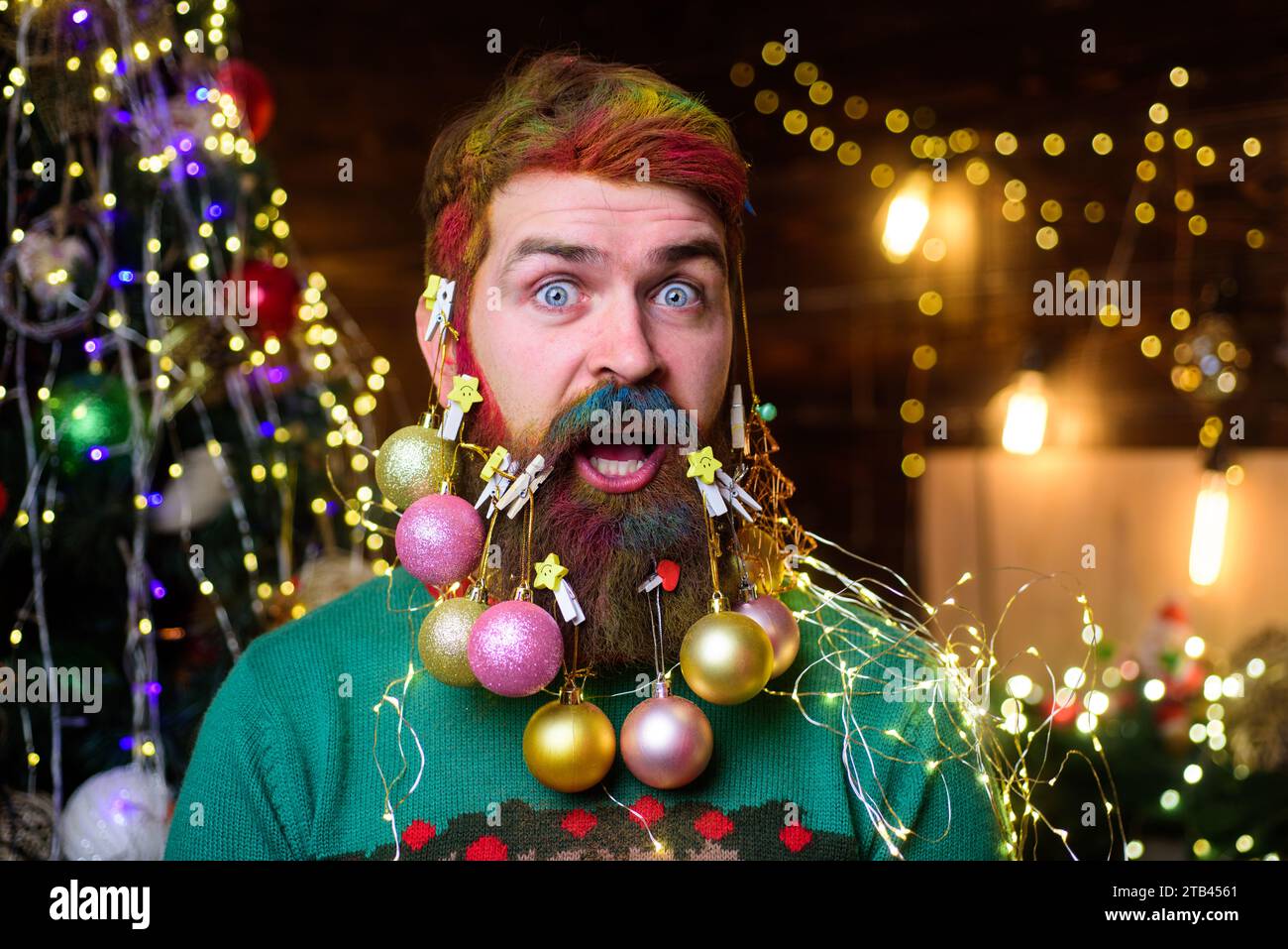 Frohe Weihnachten und frohes neues Jahr. Nahaufnahme Porträt eines überraschten Mannes mit dekorativen Kugeln im Bart. Bärtiger Mann mit verziertem Bart für Stockfoto
