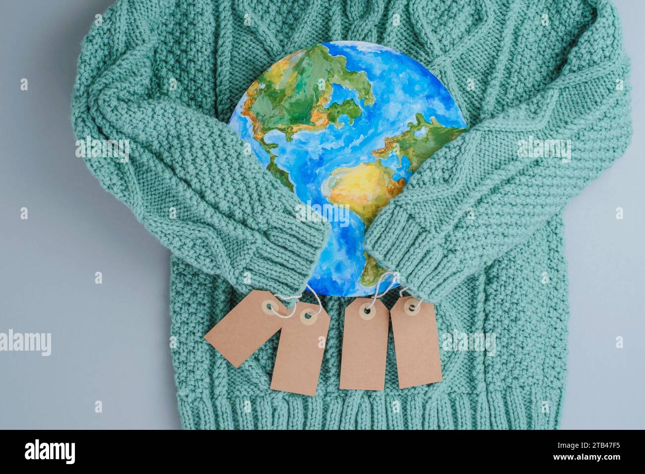 Ärmel aus Strickpullover umarmen den Planeten mit Tags. Kleidung für verantwortungsbewussten Konsum. Umweltfreundlichkeit und nachhaltige Mode. Stockfoto