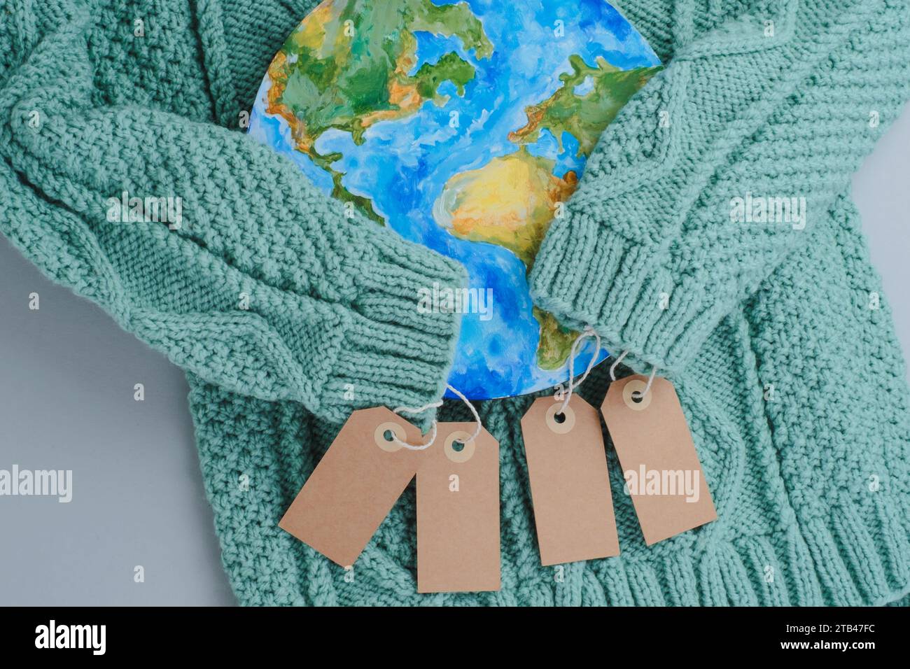 Ärmel aus Strickpullover umarmen den Planeten mit Tags. Kleidung für verantwortungsbewussten Konsum. Umweltfreundlichkeit und nachhaltige Mode. Stockfoto